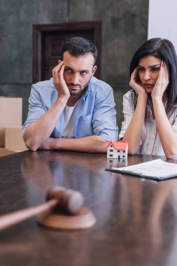 Selective focus of upset bankrupts at table with house model, documents and gavel in room clipart