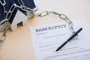 High angle view of house model with chain near pen and document with bankruptcy and chapter 13 lettering on beige clipart