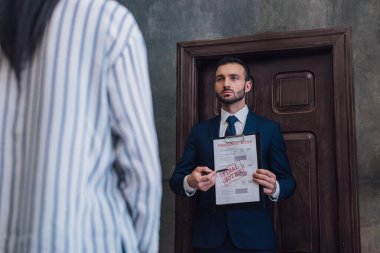 Collector pointing with pen at documents with foreclosure and final notice lettering in front of woman in room clipart