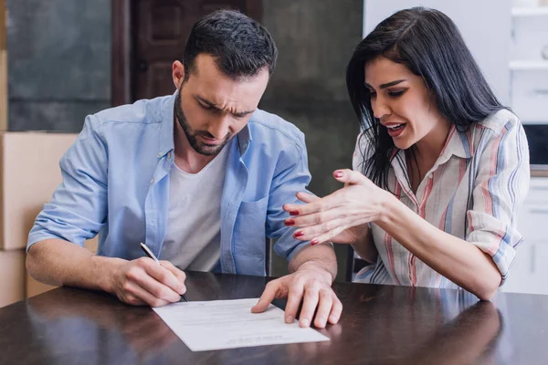 Mujer Estresada Preocupada Cerca Hombre Escribiendo Documento Mesa Habitación — Foto de Stock