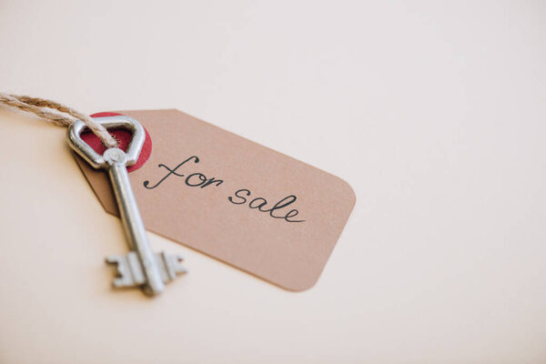 High angle view of key with trinket with for sale lettering on white background