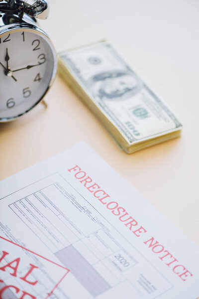 High angle view of document with foreclosure lettering near dollar banknotes and alarm clock on white