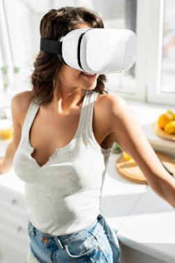 Smiling woman using virtual reality headset in kitchen  clipart