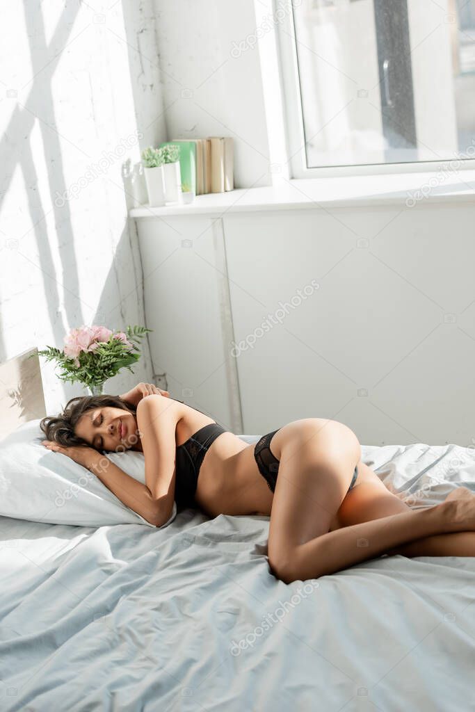 Beautiful woman in lingerie lying on bed in sunlight bedroom