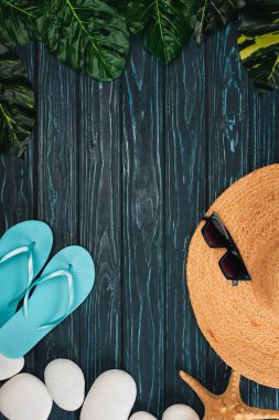 Top view of flip flops, straw hat near sunglasses and sea stones on dark wooden surface clipart
