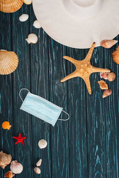 Вид сверху солнцезащитной шляпы у моря и медицинской маски на темной деревянной поверхности
