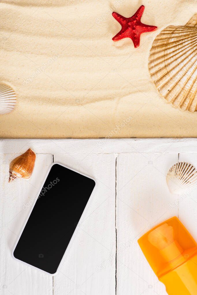 Top view of smartphone near sunscreen on white wooden planks and seashells on sand