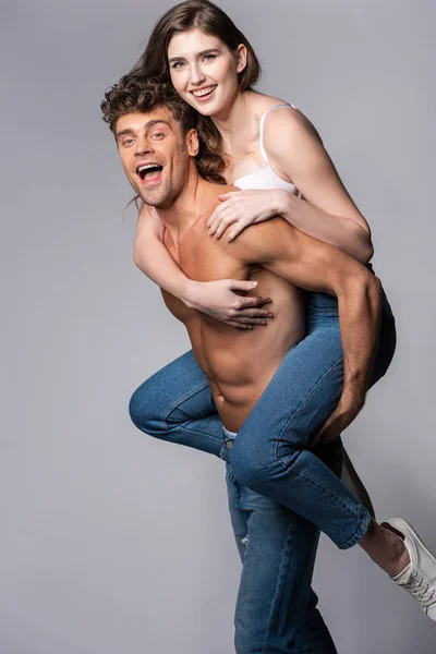 Excited Muscular Man Piggybacking Happy Girlfriend Grey — Stock Photo, Image