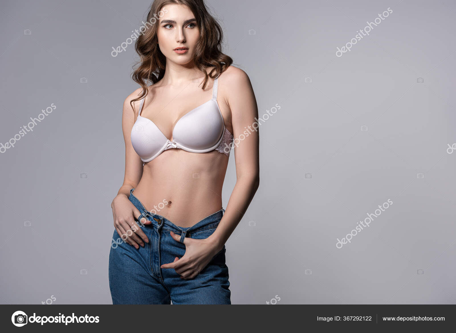 A beautiful young woman standing in a bra with big boobs holding