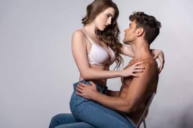 Sütyen giyen baştan çıkarıcı kızın profili gri kot pantolonlu kaslı adamın üzerinde oturuyor. 