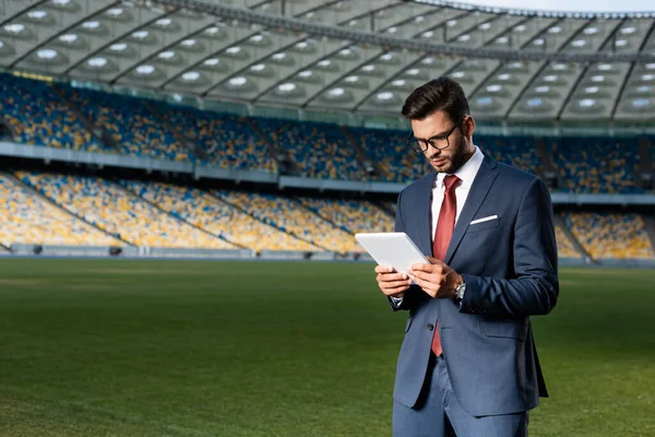 スタジアムでデジタルタブレットを使ってスーツや眼鏡を身に着けている若いビジネスマン — ストック写真