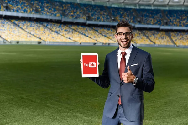 Kyiv Ukraine June 2019 快乐的年轻商人 身穿西服 戴着眼镜 手持装有Youtube应用程序的数码平板电脑 在体育场展示大拇指 — 图库照片