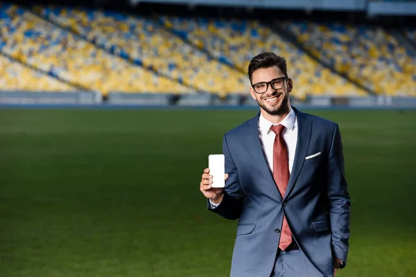 Jovem Empresário Sorridente Terno Óculos Segurando Smartphone Com Tela Branco — Fotografia de Stock