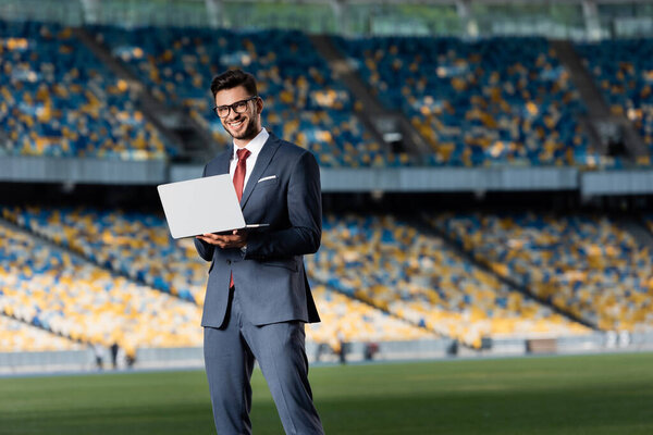 smiling young businessman in suit with laptop at stadium