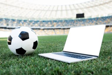 Stadyumdaki çimenli futbol sahasında boş ekranlı futbol topu ve laptop.