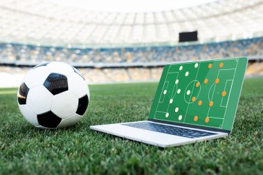 Futbol topu ve dizüstü bilgisayar stadyumdaki çimenli futbol sahasında formasyon.