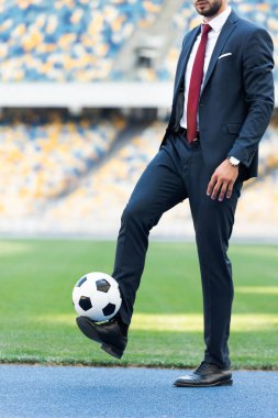 Stadyumda futbol topuyla oynayan takım elbiseli genç işadamının kırpılmış manzarası.