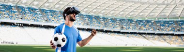 VR kulaklıklı profesyonel futbolcu bağırarak ve evet işareti yaparak stadyumda, panoramik çekim