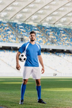Stadyumdaki futbol sahasında mavi ve beyaz formalı profesyonel futbolcu.