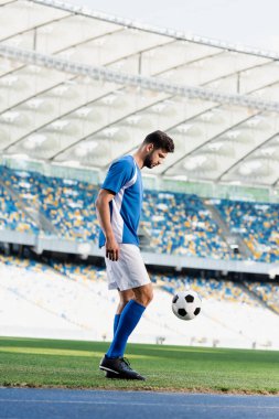 Futbol sahasında futbol sahasında mavi beyaz üniformalı profesyonel futbolcunun yan görüntüsü