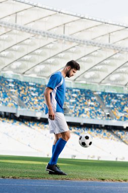 side view of professional soccer player in blue and white uniform with ball on football pitch at stadium clipart