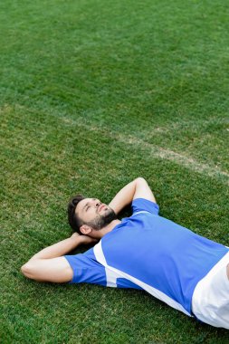Stadyumdaki futbol sahasında yatan mavi beyaz üniformalı profesyonel futbolcu.