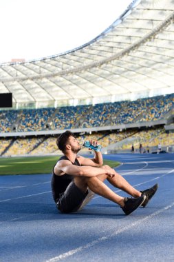 Yakışıklı sporcu stadyumda dinleniyor ve su içiyor.