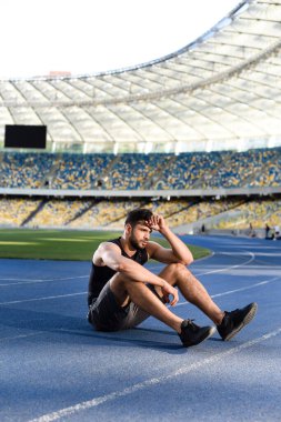 Stadyumdaki koşu pistinde dinlenen yorgun yakışıklı sporcu.