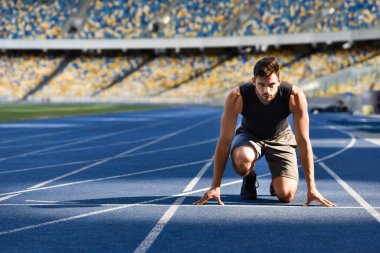 handsome runner in start position on running track at stadium clipart