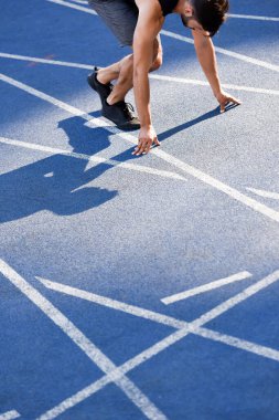 cropped view of handsome runner in start position on running track at stadium clipart