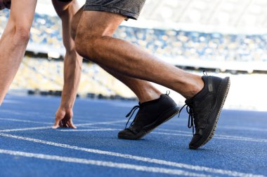 cropped view of runner in start position on running track at stadium clipart