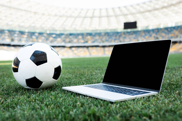 soccer ball and laptop with blank screen on grassy football pitch at stadium