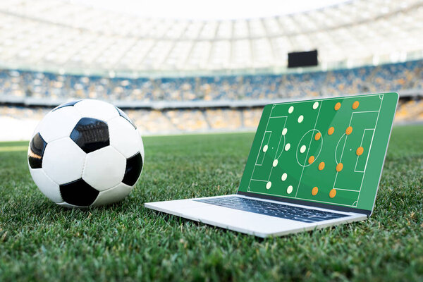 футбольный мяч и ноутбук с образованием на экране на травяном футбольном поле на стадионе
