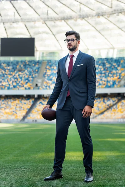 若いビジネスマンがスーツ姿でスタジアムでラグビーボールを手に — ストック写真