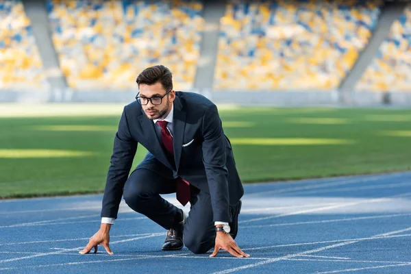 young businessman in suit in start position on running track at stadium