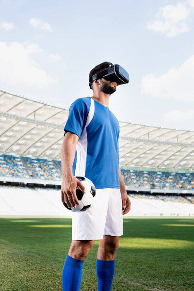 professional soccer player in vr headset and blue and white uniform with ball on football pitch at stadium
