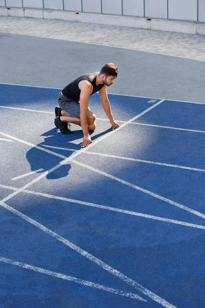 英俊潇洒的赛跑选手在体育场跑道上的起跑位置 — 图库照片