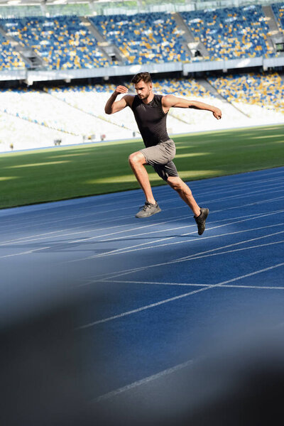 selective focus of fast handsome runner exercising on running track at stadium