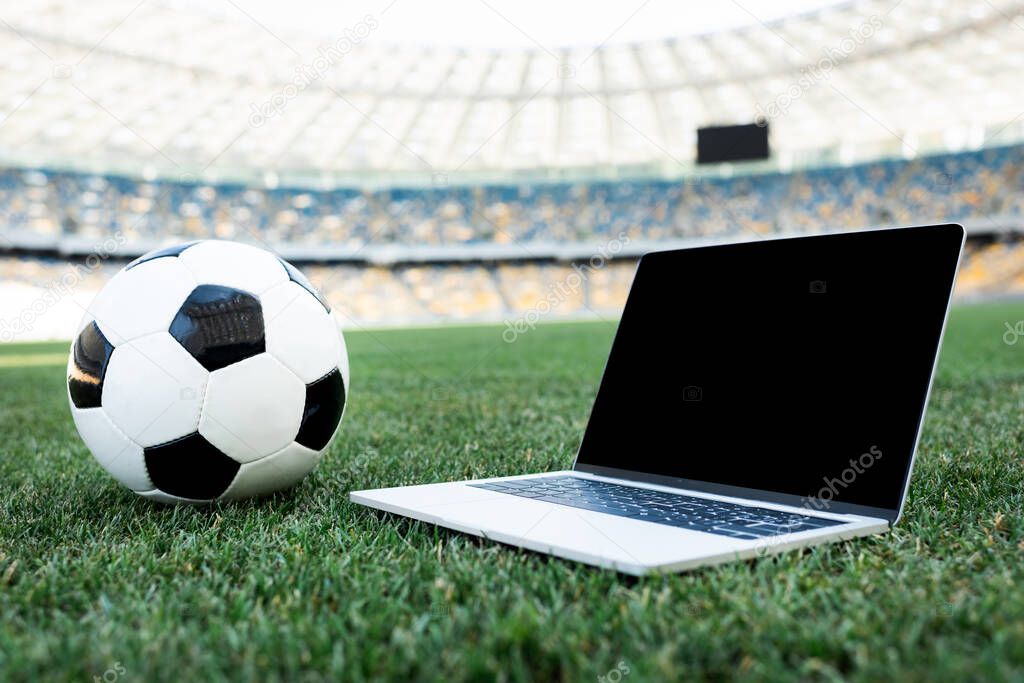 soccer ball and laptop with blank screen on grassy football pitch at stadium