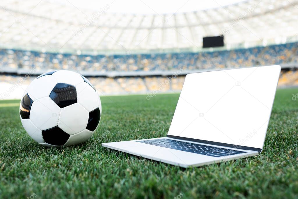 soccer ball and laptop with blank screen on grassy football pitch at stadium