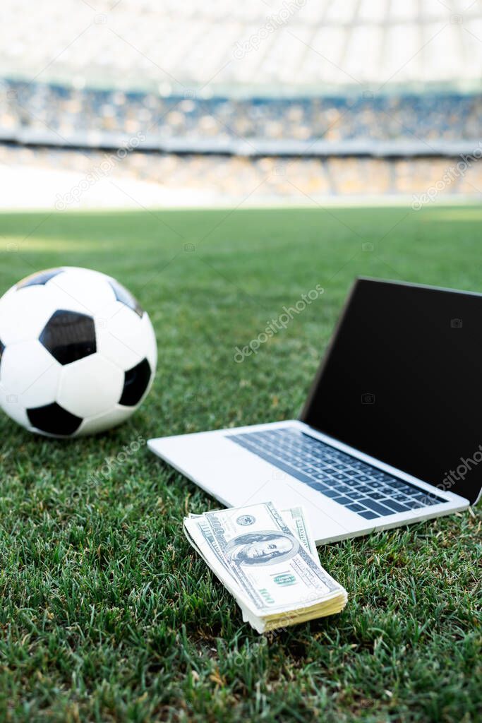 soccer ball, money and laptop with blank screen on grassy football pitch at stadium, online betting concept