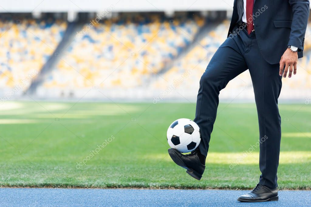 cropped view of young businessman in suit playing with soccer ball at stadium