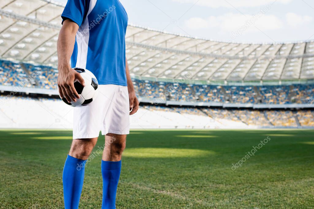 cropped view of professional soccer player in blue and white uniform with ball on football pitch at stadium