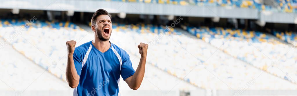 emotional professional soccer player in blue and white uniform showing yes gesture at stadium, panoramic shot