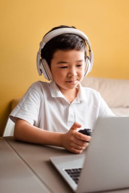 KYIV, UKRAINE - 22 Nisan 2020: Asyalı çocuk joystick ve dizüstü bilgisayarla oyun oynuyor