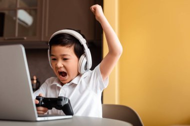 KYIV, UKRAINE - 22 Nisan 2020: bağıran Asyalı çocuk joystick ve dizüstü bilgisayarla oyun oynuyor