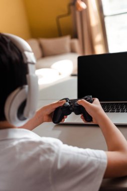 KYIV, UKRAINE - 22 Nisan 2020: karantinada boş ekranlı bilgisayar ve joystick ile video oyunu oynayan küçük çocuğun görüntüsü