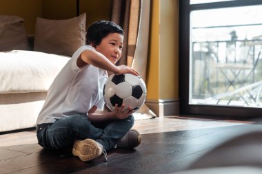 Karantinada futbol topuyla evde maç izleyen Asyalı çocuk.