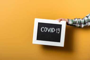 Kendini izolasyon sırasında sarının üzerinde covid-19 işareti olan tahtayı tutan çocuk görüntüsü.