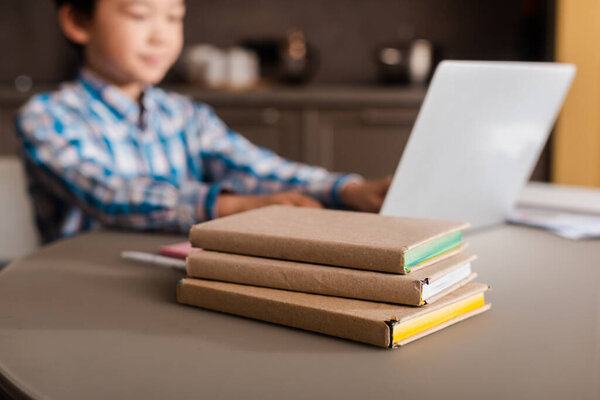 asian boy studying online with laptop and books at home during quarantine, selective focus